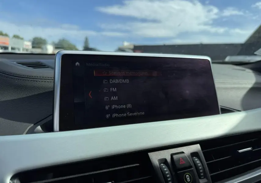 Écran multimédia central affichant les options radio dans l'habitacle d'une BMW X2 jaune vue de face intérieure.