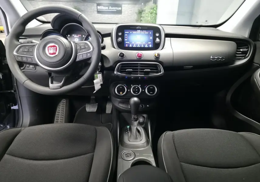 Intérieur de la Fiat 500X 2024 en vue frontale, tableau de bord gris titane avec écran tactile et volant Soft-Touch noir.