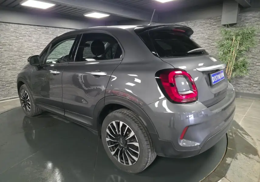 Fiat 500X gris vue 3/4 arrière droit, jantes alliage 17'', feux arrière LED, dans un showroom intérieur.