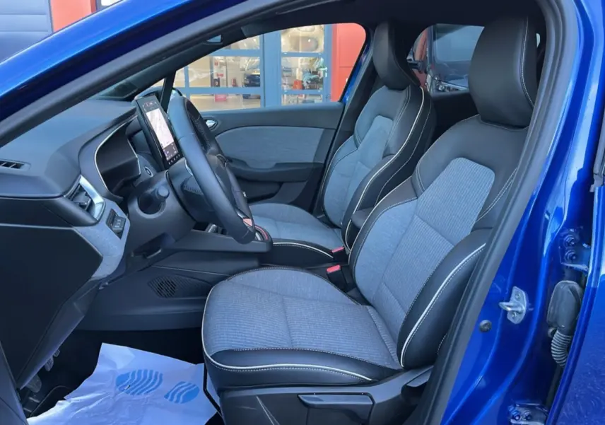 Intérieur avant droit de la Renault Clio 2025 bleu iron, sièges tissu gris et cuir noir avec surpiqûres blanches.