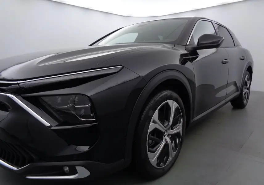 Vue 3/4 avant droit d'une Citroën C5 X noire métal avec phares fins et jantes bi-ton distinctives.