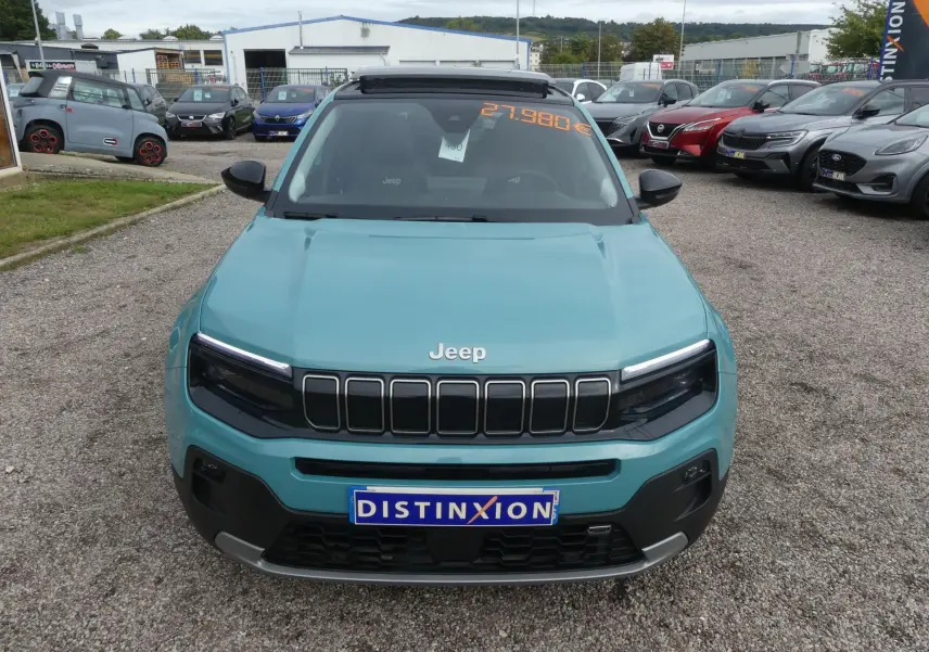 Vue frontale d'un Jeep Avenger bleu métallisé avec calandre noire et plaque Distinxion sur un parking.