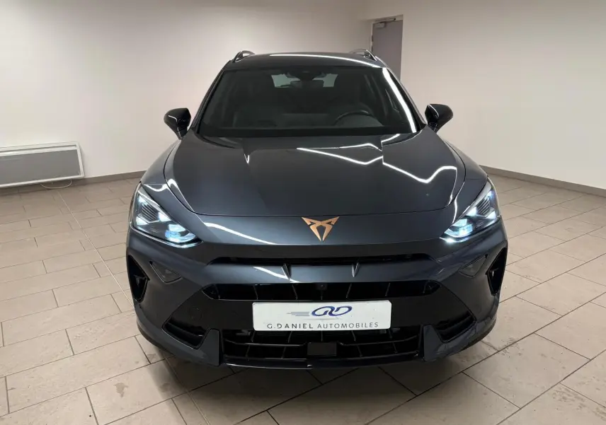 Vue frontale d'un CUPRA Formentor gris magnétique avec phares allumés et logo cuivré sur le capot.