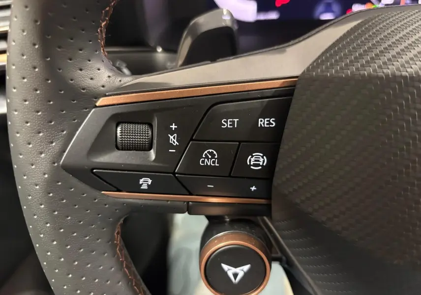 Gros plan sur les commandes du volant perforé avec logo CUPRA, soulignant les fonctions d'assistance à la conduite.