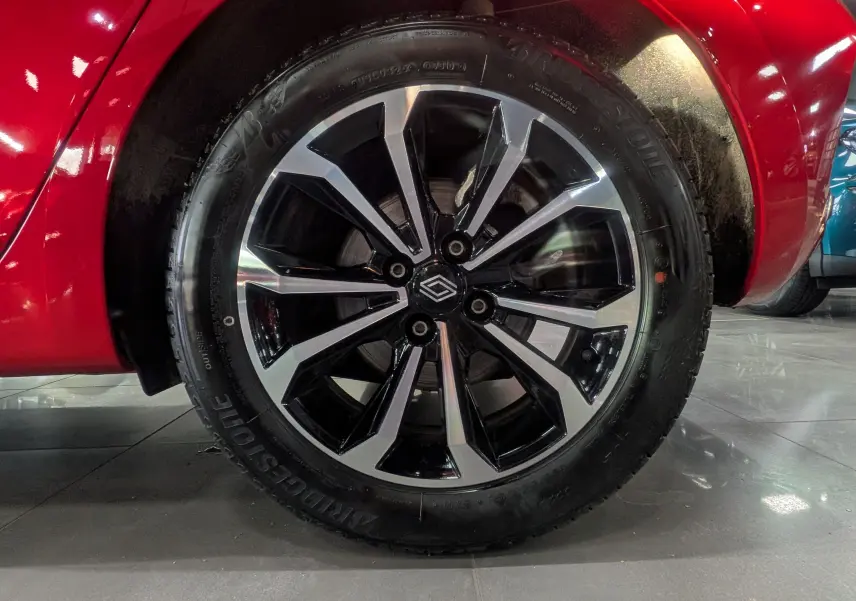 Gros plan sur la roue avant gauche de la Renault Clio V Rouge Flamme, mettant en valeur la jante noire et argentée au design moderne.