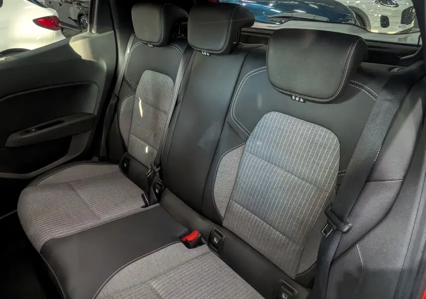 Vue intérieure arrière de la Renault Clio V rouge Flamme, montrant les sièges arrière en tissu gris et cuir noir.