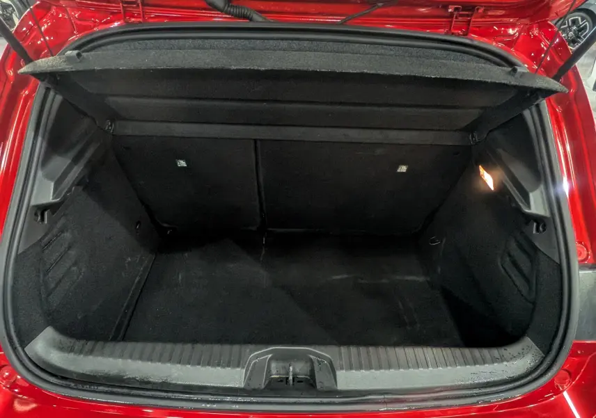 Coffre ouvert vu de l'arrière d'une Renault Clio V Rouge Flamme, montrant l'espace de chargement vide et la lumière intérieure allumée.
