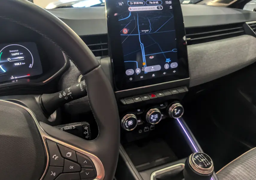 Vue intérieure centrée sur le tableau de bord et la console centrale de la Renault Clio V avec écran tactile et levier de vitesses manuel.