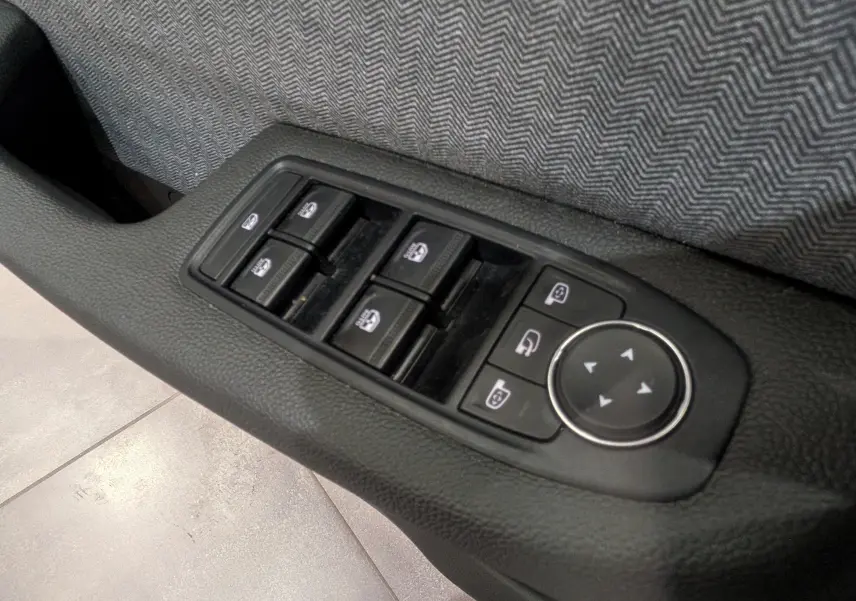 Gros plan sur les commandes des vitres et rétroviseurs côté gauche intérieur de la Renault Clio V rouge Flamme 2025.