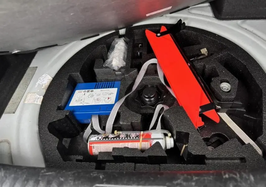 Coffre ouvert d'une Volkswagen Golf VI Cabriolet blanc, vue sur le kit de réparation pneu avec compresseur et cric rouge.