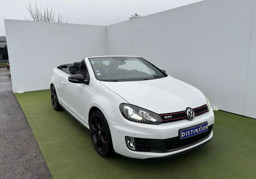 Volkswagen Golf VI Cabriolet blanc vue 3/4 avant avec jantes noires et toit ouvert sur fond neutre.