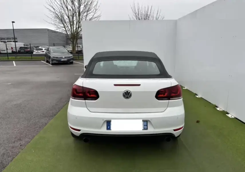 Vue arrière d'une Volkswagen Golf VI Cabriolet blanche avec toit souple noir et feux arrière teintés à LED.
