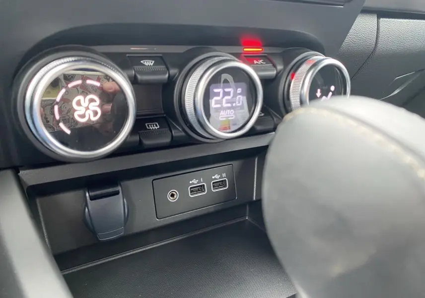 Gros plan sur la console centrale du Renault Arkana 2024 noir, montrant les commandes de climatisation et ports USB.