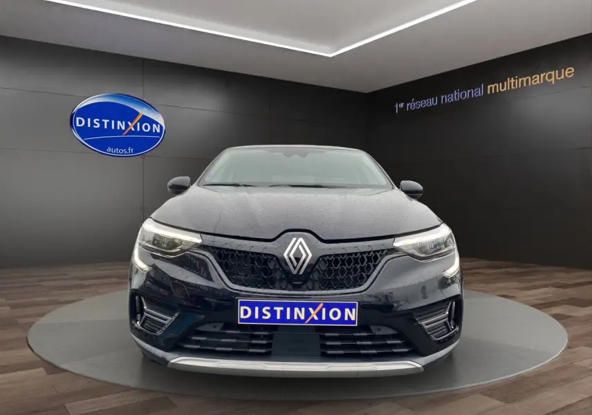 Vue avant d'un Renault Arkana noir 2024 avec calandre hexagonale et phares LED allumés en intérieur showroom.