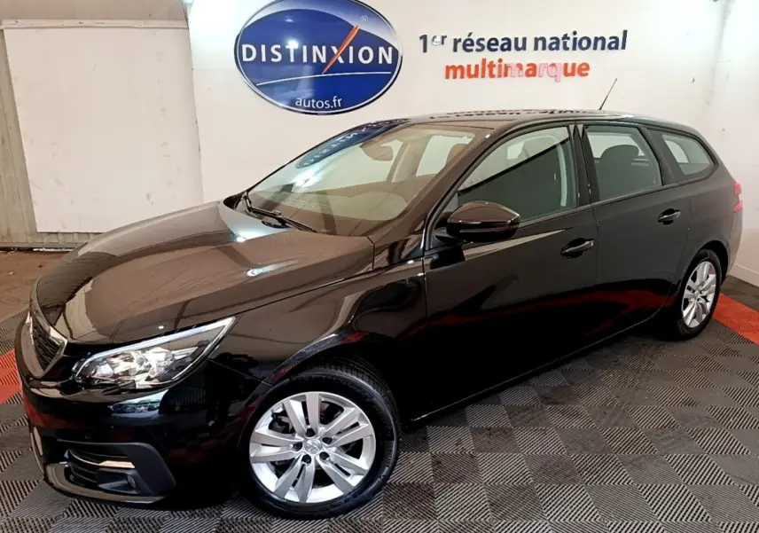 Peugeot 308 noire en break vue 3/4 avant droit dans un showroom avec sol à damier.