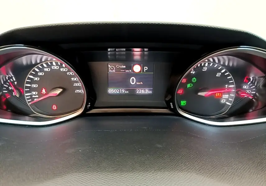 Vue rapprochée du tableau de bord numérique de la Peugeot 308 noir, affichant la vitesse à 0 km/h et divers voyants allumés.