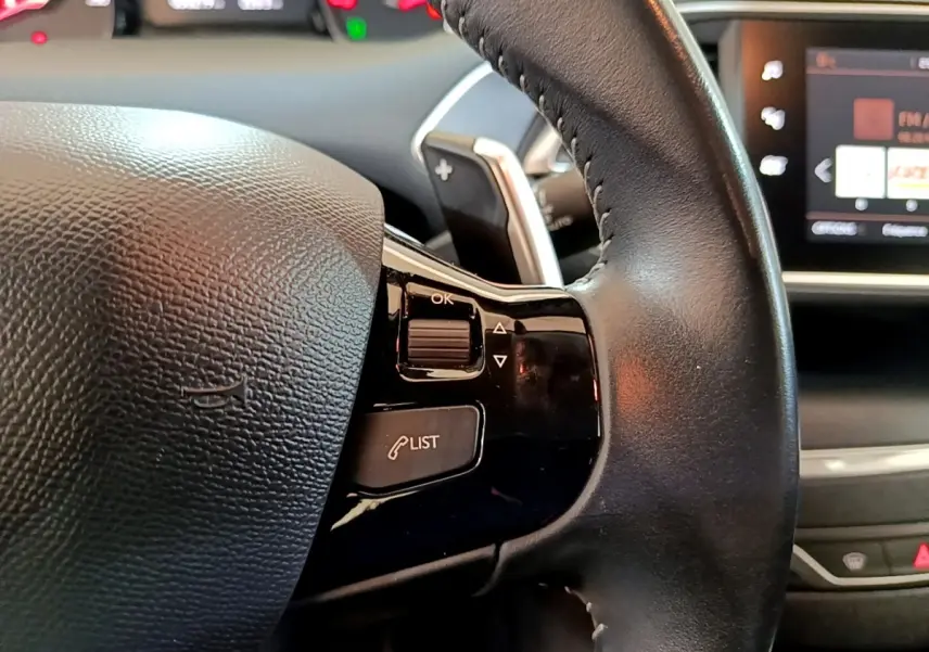 Gros plan sur le volant cuir noir de la Peugeot 308 2020 avec commandes intégrées et écran tactile en arrière-plan.