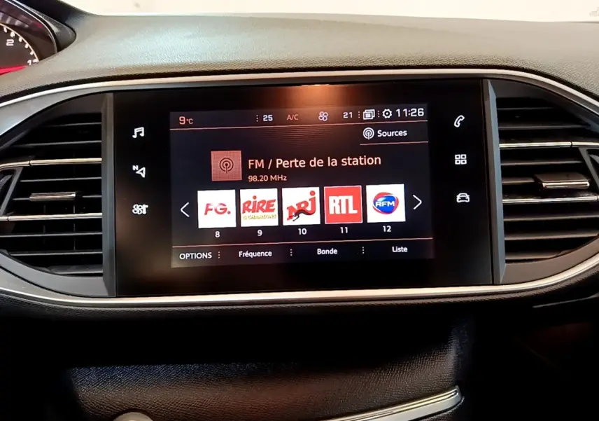 Vue rapprochée de l’écran tactile central du tableau de bord de la Peugeot 308 noire, affichant les stations radio FM.
