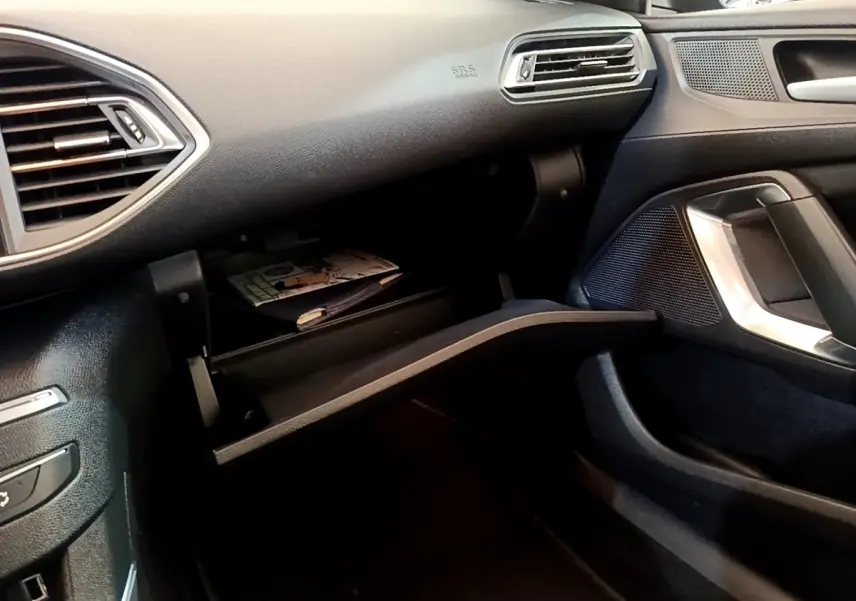 Vue intérieure côté passager de la Peugeot 308 2020, boîte à gants ouverte avec documents visibles, ambiance noire.