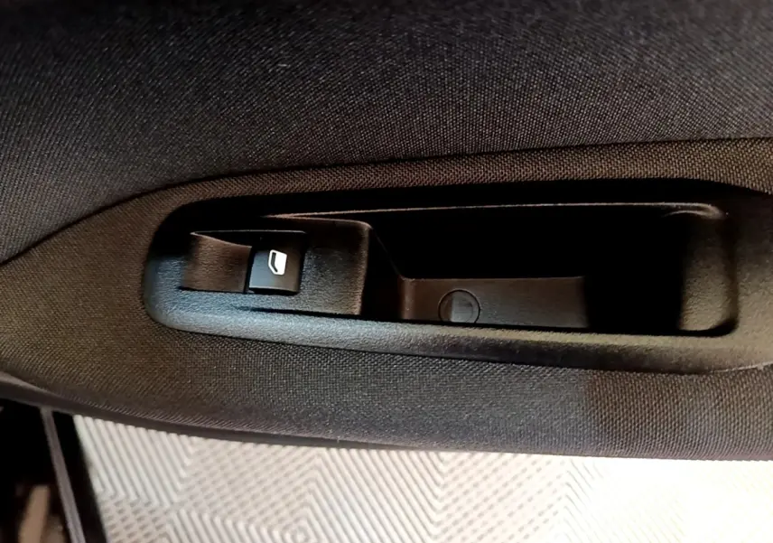 Détail de la commande d’ouverture de vitre électrique sur la porte intérieure d’une Peugeot 308 noire de 2020.