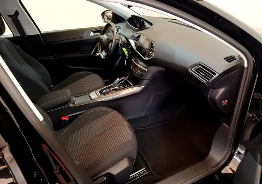 Intérieur avant droit de la Peugeot 308 noire, montrant sièges tissu, tableau de bord et console centrale avec boîte auto.