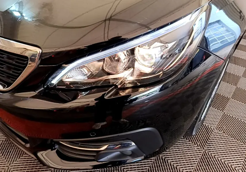 Gros plan sur le phare avant droit d'une Peugeot 308 noire, mettant en valeur les feux à LED et la calandre brillante.