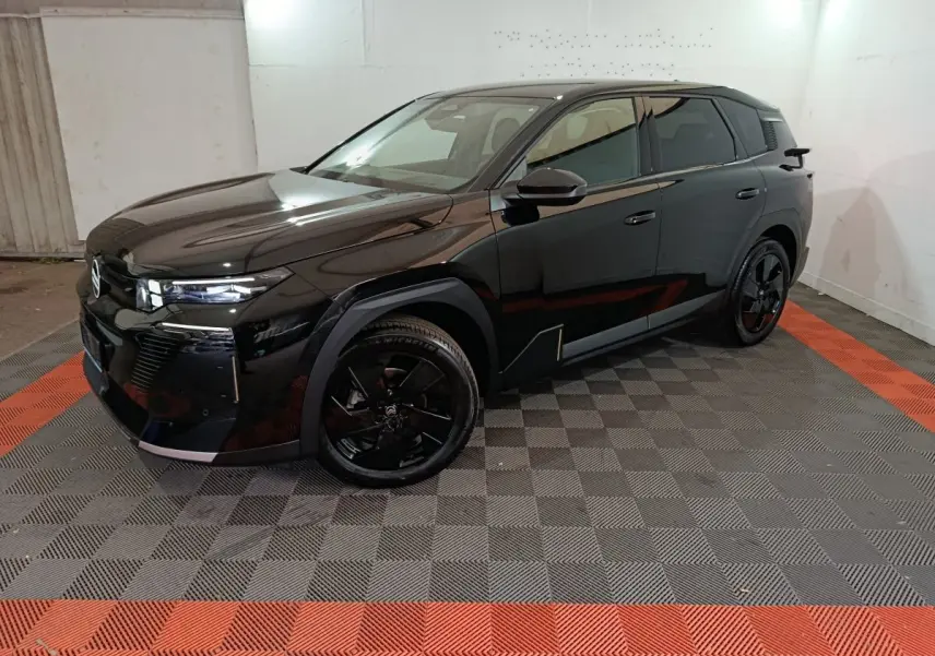 Vue 3/4 avant droite d'une Citroën C5 Hybride noire avec jantes noires et phares LED dans un garage.