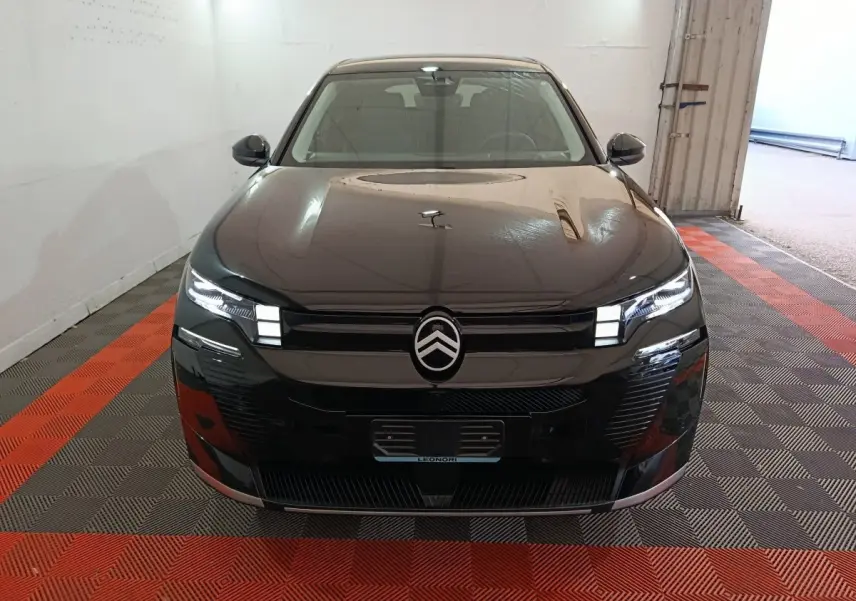 Vue avant d'une Citroën C5 hybride noire avec phares LED allumés dans un garage au sol carrelé rouge et gris.