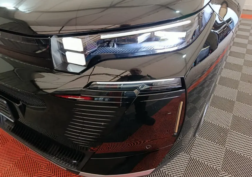 Gros plan sur le phare avant droit noir brillant du Citroën C5 Hybride 2026 avec détails LED et reflets.
