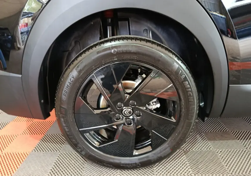 Gros plan sur la roue avant gauche noire avec jante en alliage noir brillant et logo Citroën au centre.