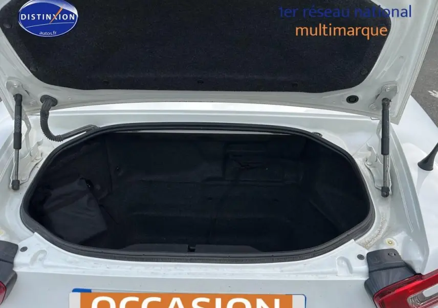 Coffre ouvert vu de dessus sur une FIAT 124 Spider blanc, montrant l'espace de rangement vide et la garniture noire intérieure.