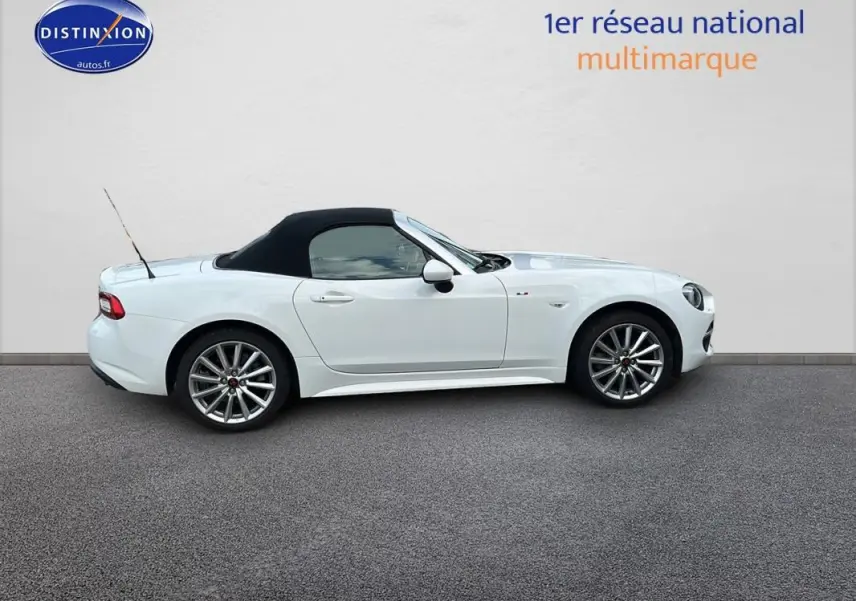 Profil côté gauche d'une FIAT 124 Spider blanc avec capote noire et jantes alliage 17 pouces sur fond neutre.