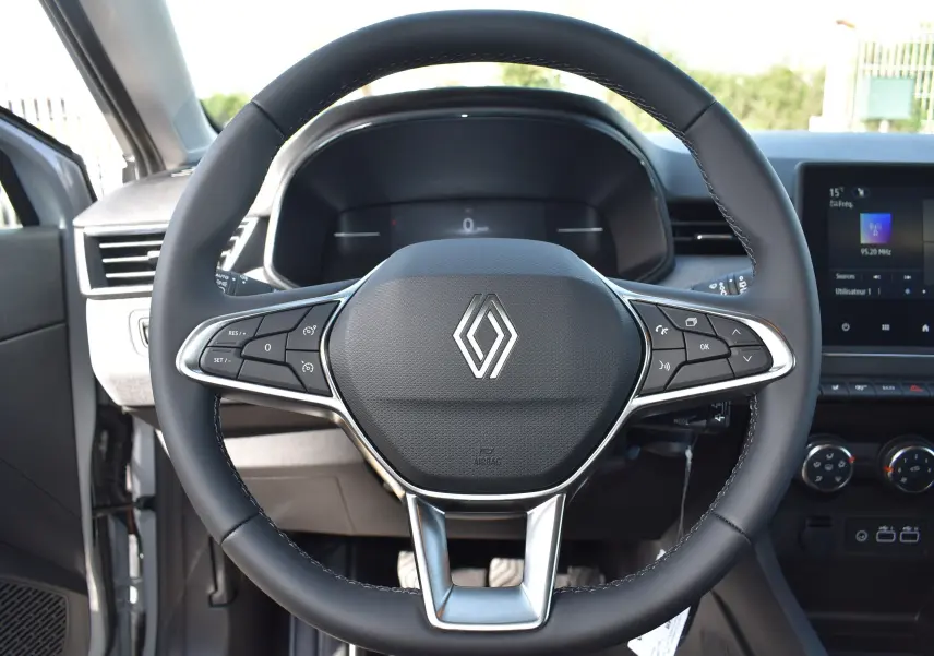 Vue rapprochée du volant noir de la Renault Clio V TCE 90 gris, avec commandes intégrées et tableau de bord digital.