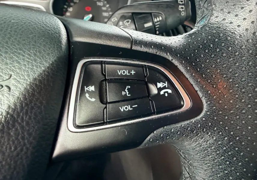 Vue intérieure côté conducteur de la Ford Focus gris 2018, montrant le volant, la boîte manuelle et les sièges tissu noirs avec surpiqûres rouges.