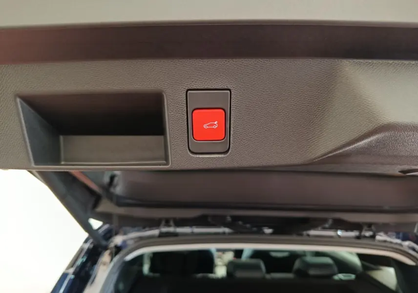 Bouton rouge d'ouverture électrique du coffre sur la trappe arrière d'une Citroën C5 Hybride noire, vue intérieure du coffre ouvert.