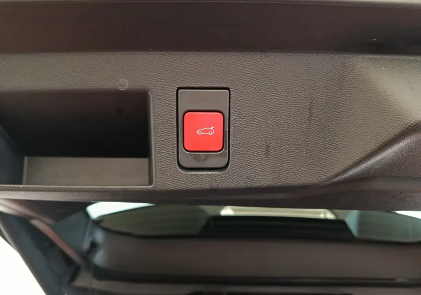 Bouton rouge d'ouverture électrique du coffre sur le panneau intérieur noir du hayon arrière du Citroën C5 Hybride.
