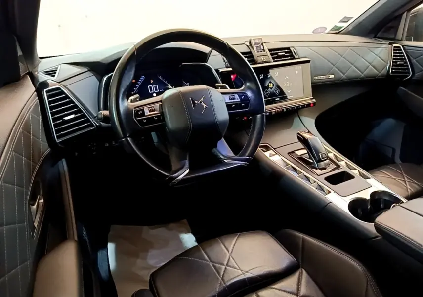 Vue intérieure du poste de conduite du DS7 Crossback avec volant cuir, tableau de bord digital et sellerie cuir matelassée noire.