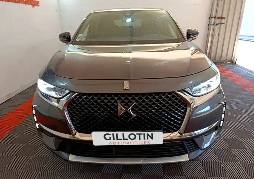 Vue avant d'un DS7 Crossback gris foncé avec calandre distinctive et phares LED allumés en intérieur.