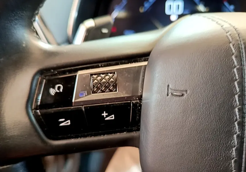 Gros plan sur les commandes du volant en cuir noir du DS7 Crossback PureTech 180, affichage digital en arrière-plan flou.