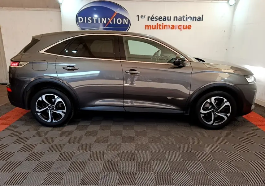 Vue latérale droite d'un DS7 Crossback gris foncé 2019, avec jantes alliage et vitres teintées, en intérieur showroom.