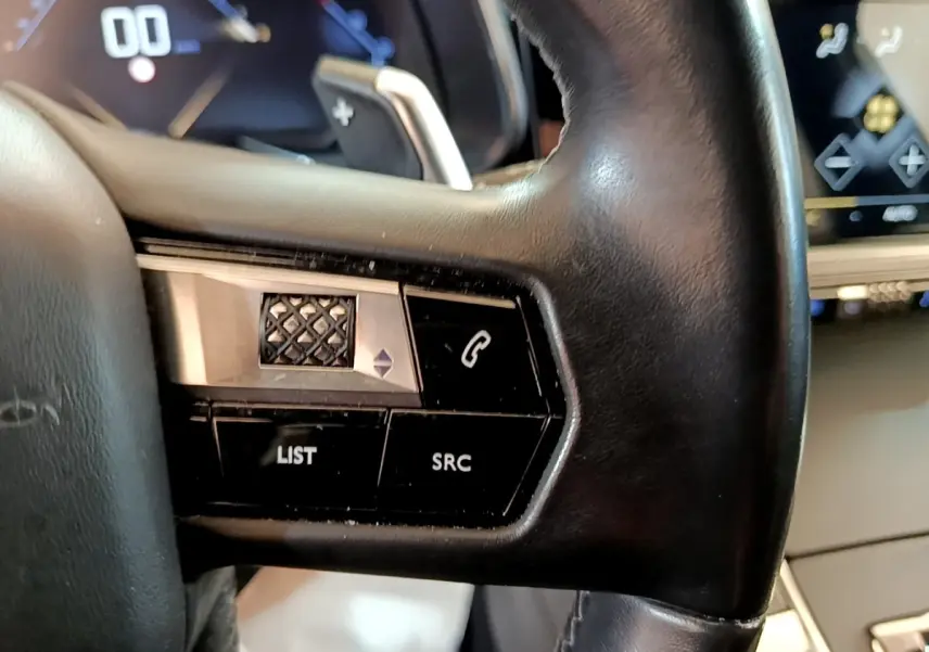 Gros plan sur le volant cuir noir du DS7 Crossback 2019, avec commandes intégrées et tableau de bord digital en arrière-plan.