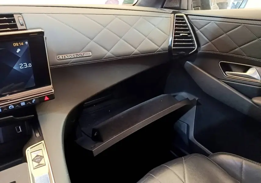 Vue intérieure côté passager du DS7 Crossback gris foncé, montrant la boîte à gants ouverte et la finition cuir matelassée.