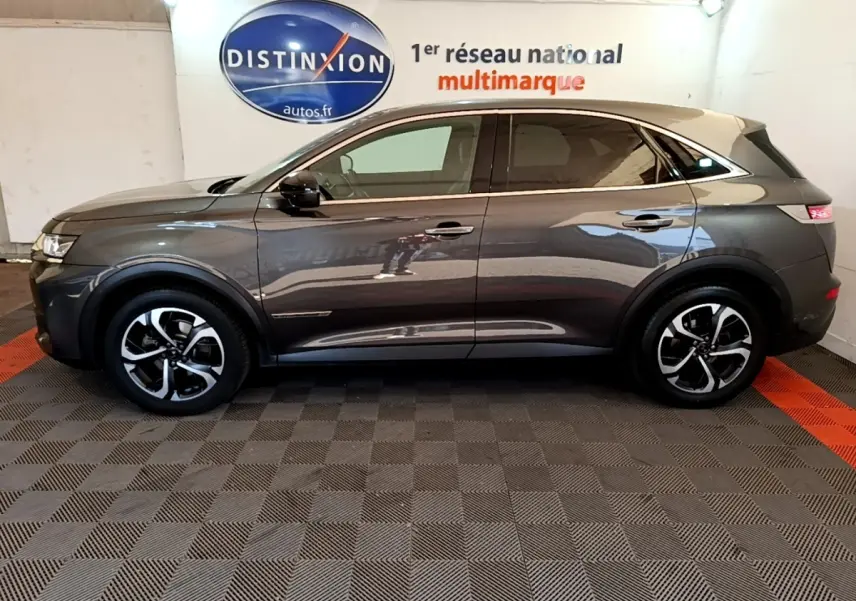 Vue de profil côté gauche d’un DS7 Crossback gris foncé avec toit clair, roues alliage et feux arrière LED visibles.