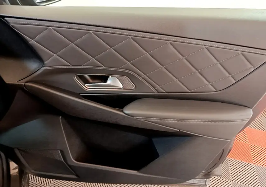 Gros plan sur la porte intérieure côté conducteur du DS7 Crossback gris foncé, avec surpiqûres en losange et poignée métal.