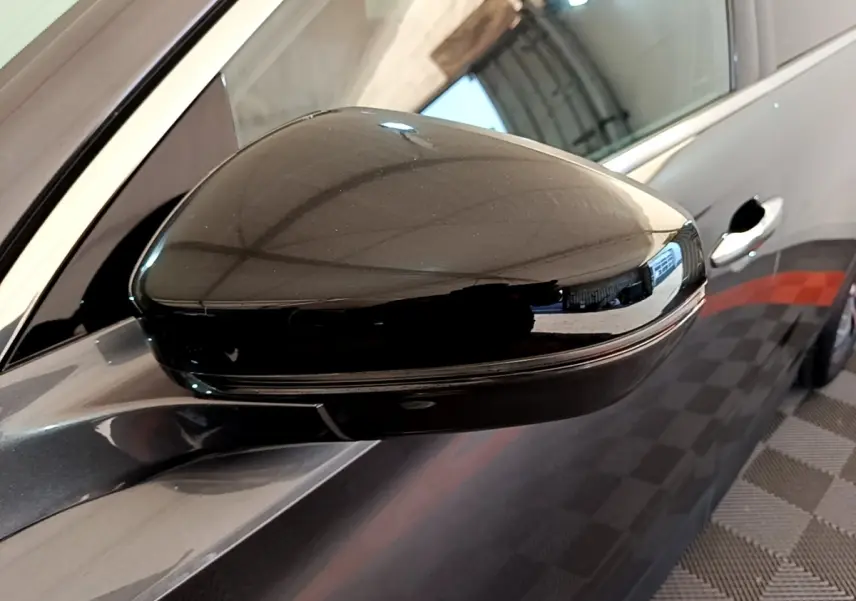 Gros plan sur le rétroviseur droit noir brillant du DS7 Crossback gris foncé, avec porte et poignée visibles en arrière-plan.
