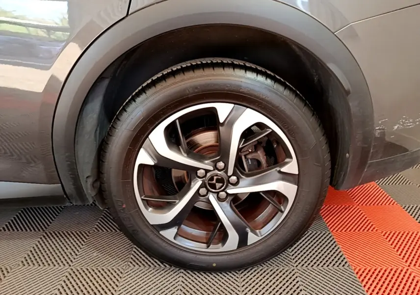 Gros plan sur la roue avant droite d’un DS7 Crossback gris foncé, mettant en valeur la jante alliage bicolore.