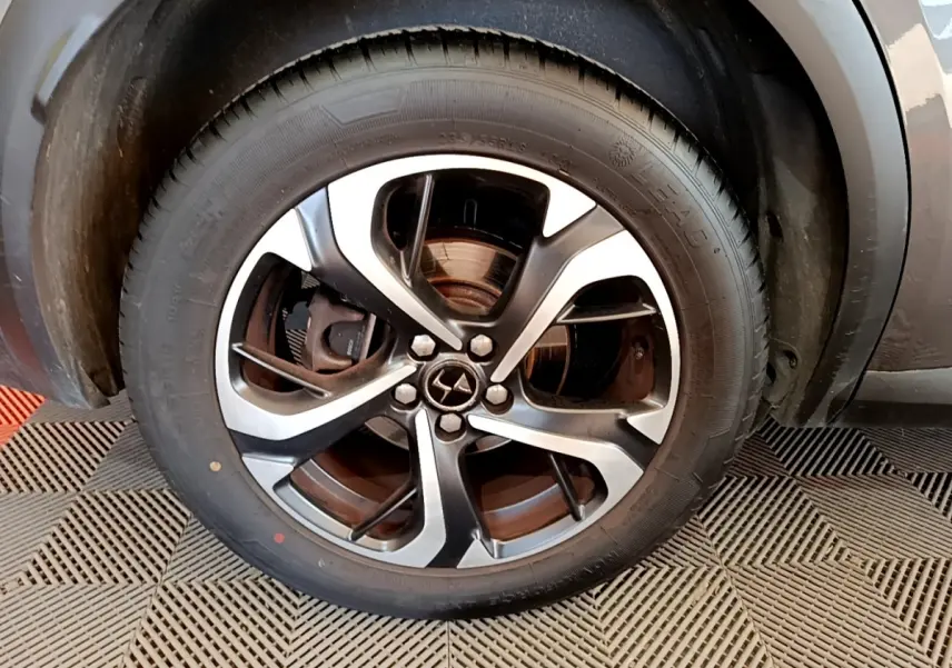 Gros plan sur la roue avant droite du DS7 Crossback gris foncé, mettant en valeur la jante alliage bicolore et le logo DS central.