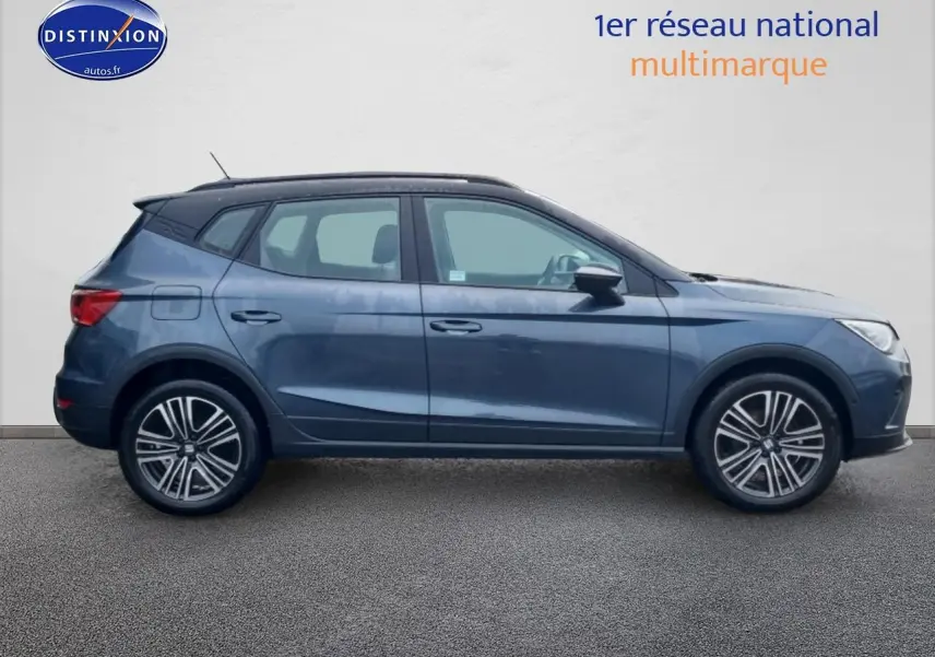 Profil droit d'un SEAT Arona gris magnétique 2025 avec jantes 17 pouces et barres de toit noires.