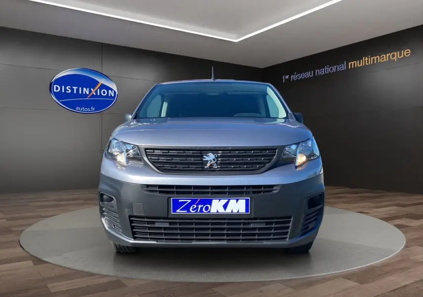 Vue frontale d'un Peugeot Partner Fourgon gris Artense métallisé avec calandre noire et plaque "Zéro KM" visible.