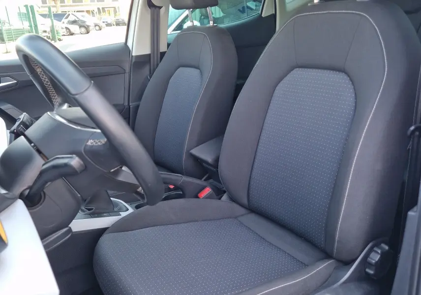 Vue intérieure côté conducteur du SEAT Arona 2025, sièges tissu noir avec surpiqûres, volant cuir multifonction visible.
